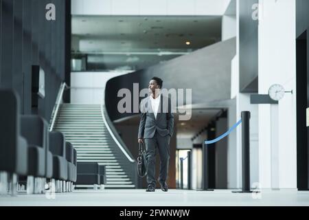 Full length portrait of successful African-American businessman walking towards camera in office building hall, copy space Stock Photo