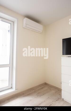 The air conditioner is installed in the corner of the real room next to the door to the balcony. The interior of the bedroom. Stock Photo