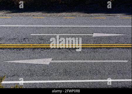 Arrows showing which direction to drive on are painted on a road in New Zealand which drives on the left side of the road.  Which way. Stock Photo