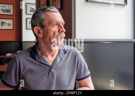An adult Caucasian senior man sits in a cafe and looks out the window Stock Photo