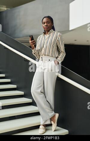 Graphic full length portrait of confident African-American woman looking at camera while posing in office hall Stock Photo