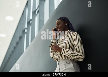 Graphic side view portrait of smiling African-American businesswoman speaking by smartphone while standing against black background Stock Photo