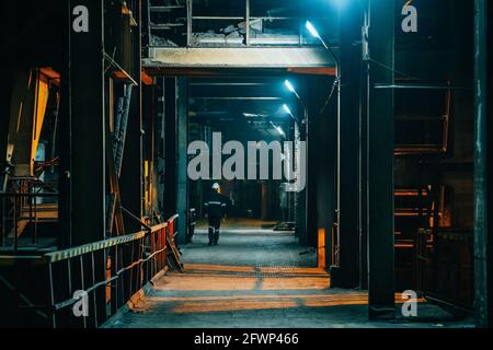 Dark creepy industrial corridor with lamp illumination and silhouette of worker man in distance. Stock Photo