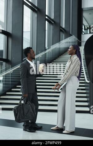 Graphic full length portrait of two African-American business people chatting cheerfully while standing in office hall Stock Photo