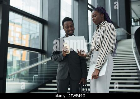 Graphic waist up portrait of two African-American business people discussing documents while standing in office hall, copy space Stock Photo