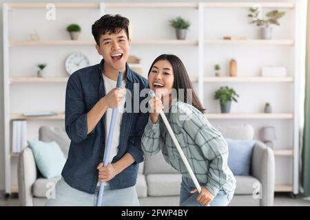 Positive chinese lovers having fun while cleaning house Stock Photo