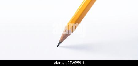 Pencil stands on white paper. The sharp point has just been sharpened. Focus on the black graphite tip. Wide background image Stock Photo