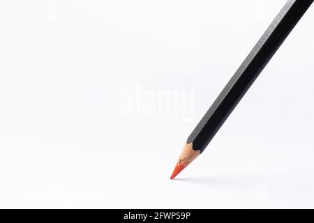 Black colored pencil with sharp red point stands on white paper. Background image Stock Photo