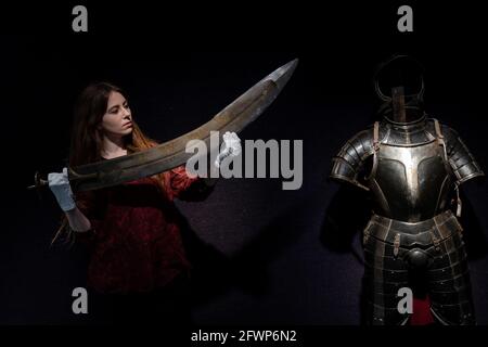 A massive Indian processional headmans sword (tegha) 19th centaury with a guide price of £4,000 - £5,000 is held next to A Composite German Black and White Three Quarter Armour Partly Third Quarter of the 16th Century and Later with a guide price of £4,000 - £5,000 , during a preview for the forthcoming Antique Arms and Armour Sale, at Bonhams' London. Picture date: Monday May 24, 2021. Stock Photo