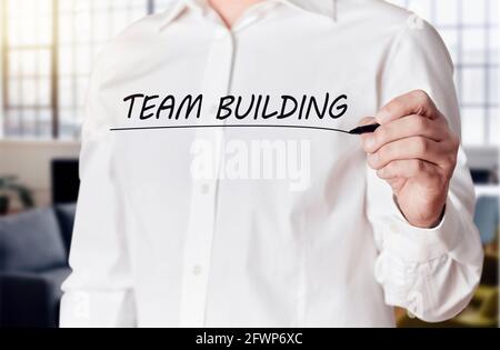 Businessman hand holds a pen and underlines the words team building on a virtual screen. Business teamwork concept. Stock Photo