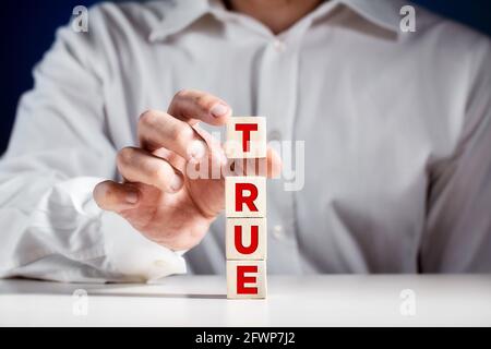 Man puts a cube on top of tiered wooden cubes with the word true. Revealing the truth concept. Stock Photo