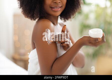 Cropped view of young black woman applying cream on her body, pampering her skin after shower at home, closeup Stock Photo