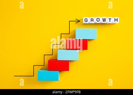 An upward pointing arrow on top of growing graph made of wooden blocks over yellow background Stock Photo