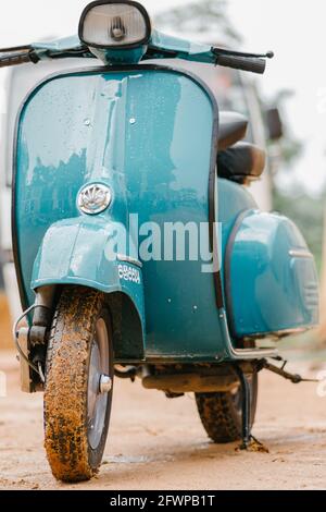 Vespa Scooter front close up view, parked in a muddy road in a rainy day. Sky blue vintage classic motor bike. Stock Photo