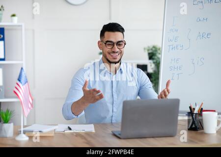 Studying English online. Cheerful Arab male teacher giving foreign language lesson on web using laptop Stock Photo