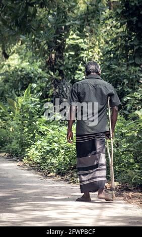 Senior adult walk with help of a stick in a lonely rural village street. Stock Photo