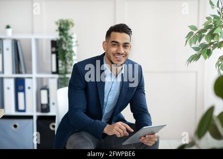 Handsome Arab businessman in formal suit using tablet pc at workplace, looking through web documents in office Stock Photo