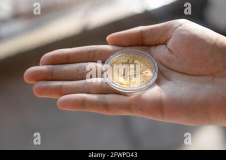 Young man holding BTC Bitcoin token on palm of hand - Cryptocurrency and Digital asset concept Stock Photo
