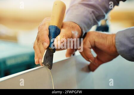 The hands of an elderly carpenter and a tool while working in close-up. Processing of a wooden plate with a cutter in a furniture shop. Close-up. working in a carpentry shop Stock Photo