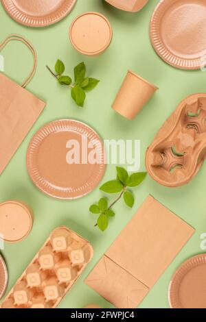 Flat lay composition with eco-friendly tableware and kraft paper food packaging on green background. Sustainable packaging, recyclable paperware, zero Stock Photo