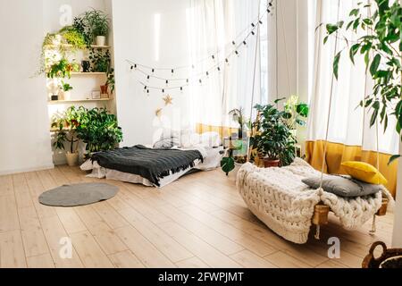 Light sofa with pillows against a gray wall. There are many pots of green plants behind the sofa. Stock Photo