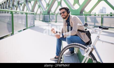 Young business man commuter with bicycle going to work outdoors in city, using smartphone. Stock Photo