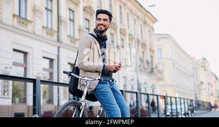 Young business man commuter with bicycle going to work outdoors in city, using smartphone. Stock Photo