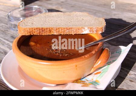 Rustic bowl of goulash soup with a slice of bread on top. (text on the napkin: 'enjoy your meal' in French and Italian) Stock Photo