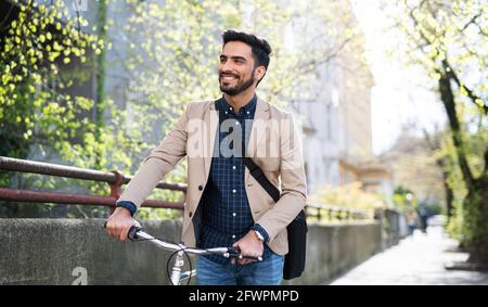 Young business man commuter with bicycle going to work outdoors in city. Stock Photo