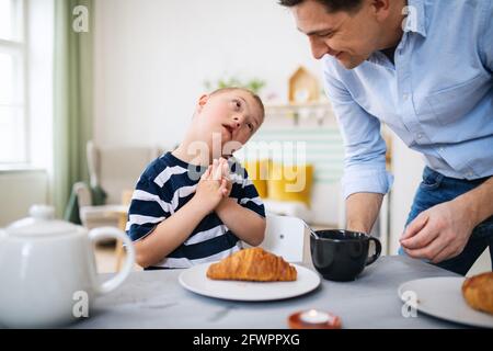 Down syndrome boy with father at the table, having breakfast. Stock Photo