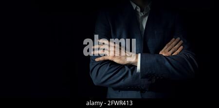businessman in suit with crossed arms standing on dark black background. copy space Stock Photo