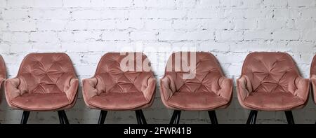 row of pink empty chairs on white brick wall background Stock Photo