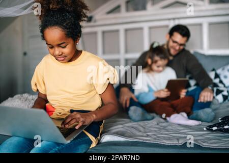 Preteen schoolgirl doing her homework with notebook at home. Child using gadgets to study. Stock Photo