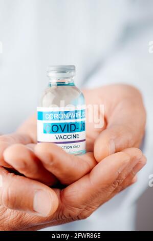 closeup of a doctor man, wearing a white lab coat, with a mock covid-19 vaccine bottle in his hands Stock Photo