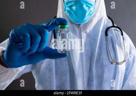 Mid section of health worker wearing protective clothes holding covid-19 vaccine bottle Stock Photo