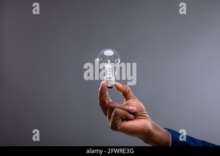 Close up of businessman holding light bulb against grey background Stock Photo