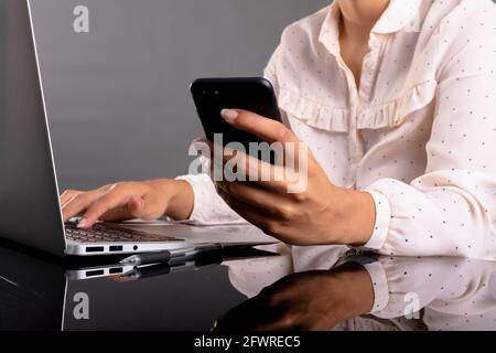 Mid section of businesswoman using laptop and smartphone against grey background Stock Photo