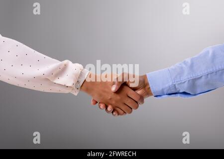 Close up of businessman and businesswoman shaking hands against grey background Stock Photo