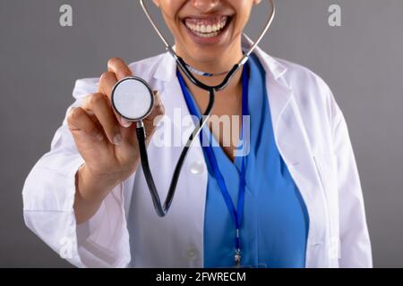 Mid section of african american female doctor holding stethoscope smiling against grey background Stock Photo