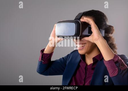 Mid section of businesswoman wearing vr headset smiling against grey background Stock Photo