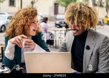 Multicultural business people sitting in a cafeteria outside drinking coffee and working with laptop. They are talking and having fun. Stock Photo