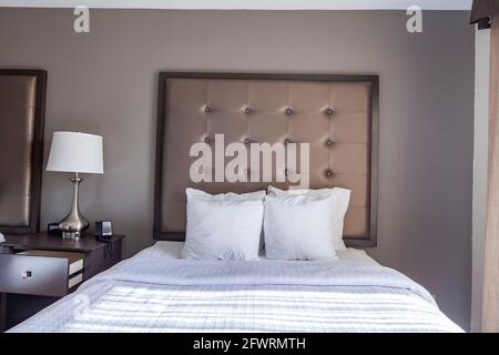 Closeup image of a ready made queen size bed with white bedding and a bunch of pillows. An upholstered head board is on the wall. A generic hotel room Stock Photo