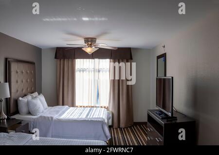 Pastel colored contemporary hotel room with flat screen tv on a  stand with chest of drawers and carpeted floors. A generic interior image where sun l Stock Photo