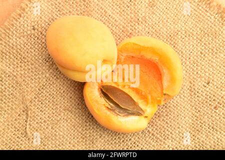 One whole and one pineapple apricot cut in half, macro, on jute fabric, top view. Stock Photo