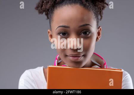 Dedicated serious young black student clutching her text books as she looks earnestly at the camera in a cropped portrait on a grey studio background Stock Photo