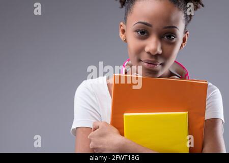 Serious responsible young Black female student clutching her books as she looks intently at the camera in a close up cropped portrait on a grey studio Stock Photo