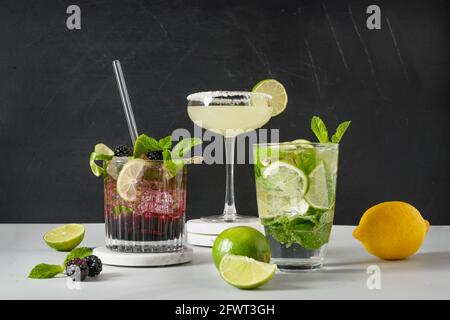 Classic and blackberry mojito, margarita cocktail with lime on black background. Three summer freshness beverage for festive party. Summer holiday moc Stock Photo