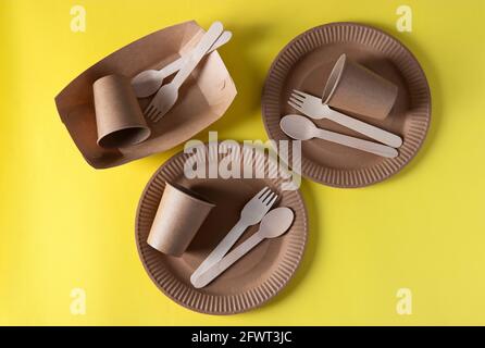 Three sets disposable biodegradable tableware of craft paper and wood - plates, forks, spoons, glasses on yellow background. Zero Waste. View from the Stock Photo
