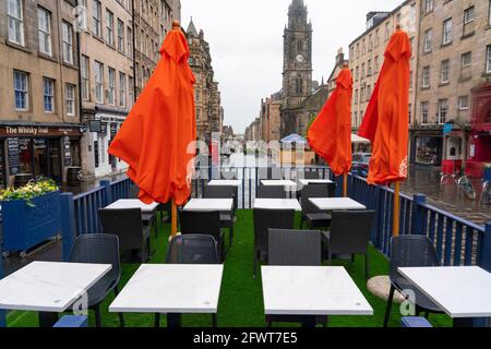Scotland, Scotland, UK. 24 May 2021. Unseasonable cool and damp weather in Edinburgh meant that there were few customers in the many outdoor bars , cafes and restaurants in the city centre, With few tourists in the capital the streets remain much quieter than normal. Pic; Outdoor seating for bars and restaurants lie empty at lunchtime on the Royal Mile. Iain Masterton/Alamy Live News Stock Photo