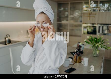 Happy woman in bathrobe and towel on head doing beauty or cosmetic procedures at home Stock Photo